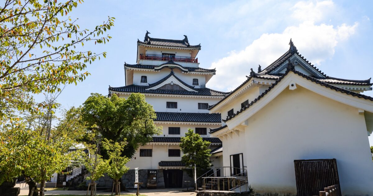青空の下に立つ唐津城と周囲の木々の風景