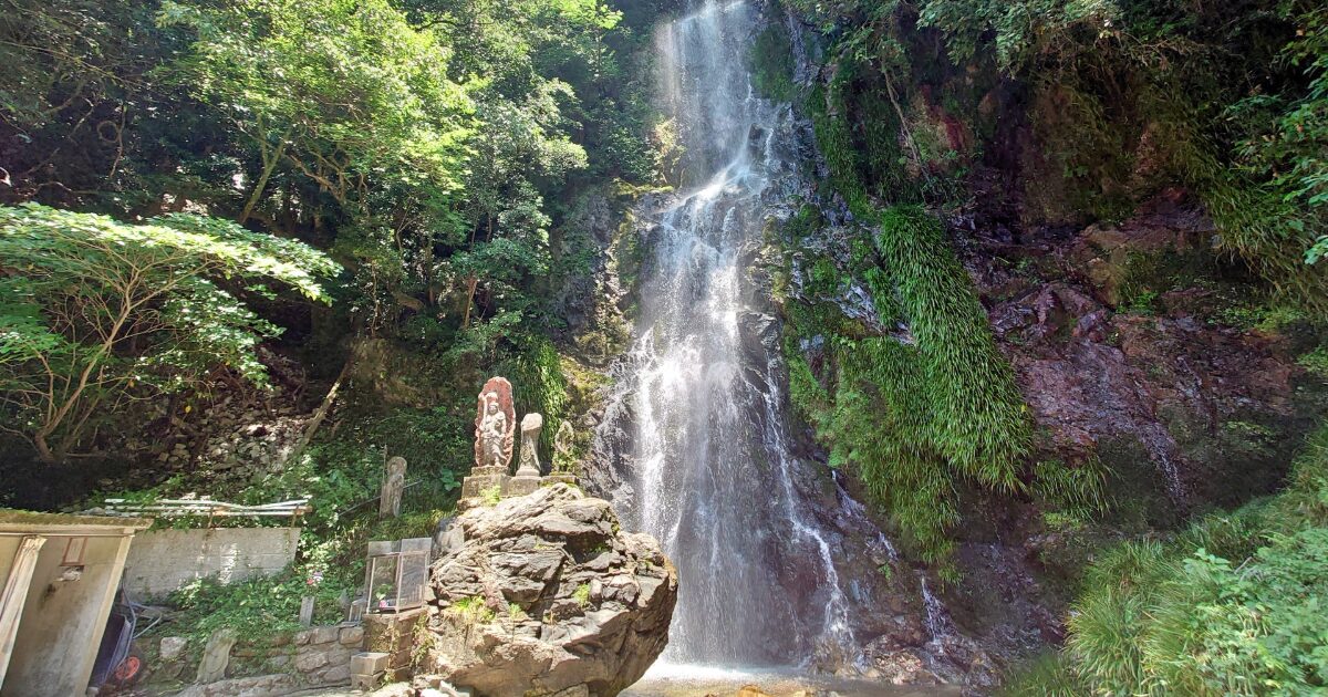 木々に囲まれた滝と石像のある自然風景